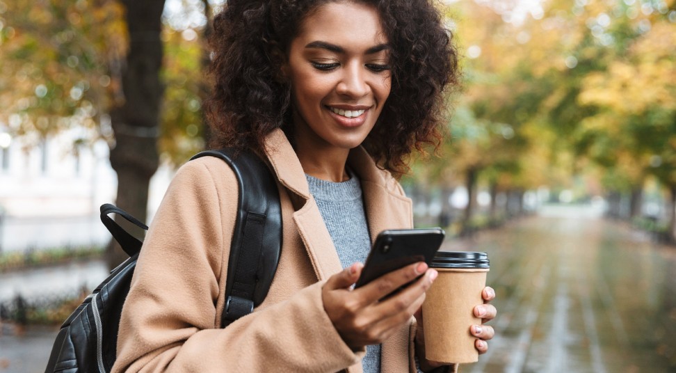 woman outside with coffee getting phone alert